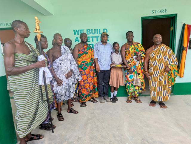 Traditional leaders and a pupil stand together in the school corridor. Hon. Thomas Worlanyo Tsekpo, MP, wears a cap.