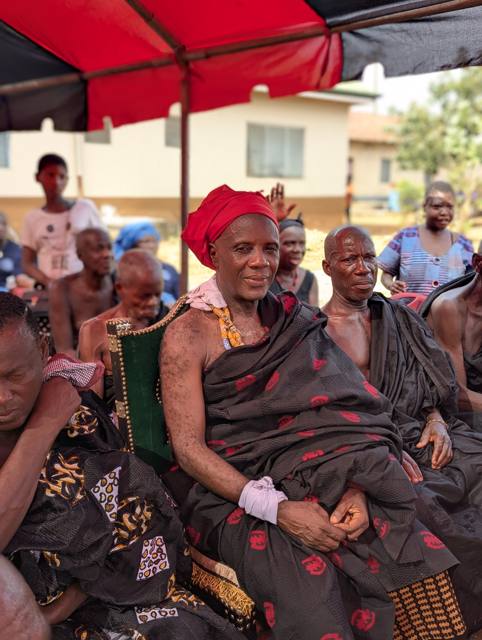 Togbe Boesi III, the Mankrado of Fodome Amele, seated in a red head cloth and amber beads on a studded chair.