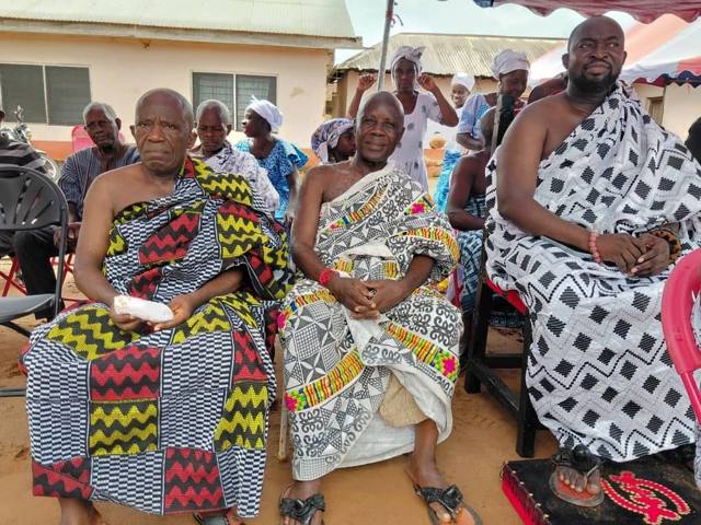 Elders seated in kente and patterned cloth under the tent.