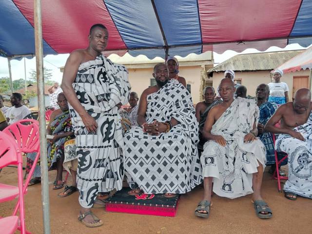 Elders seated on cushions beneath the striped tent.