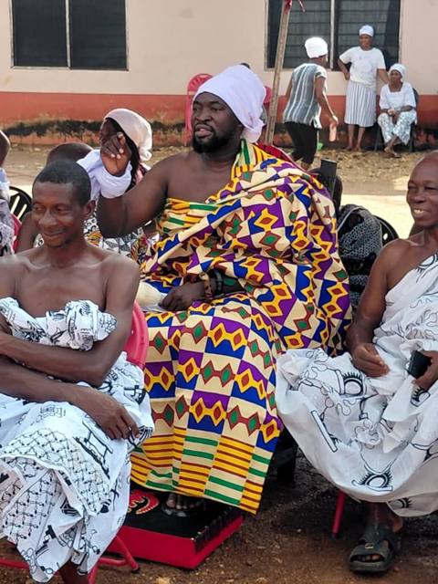 Elders and women seated beneath the striped tent.